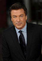 Headshot of Alec Baldwin, who is in a black suit with a shiny black tie